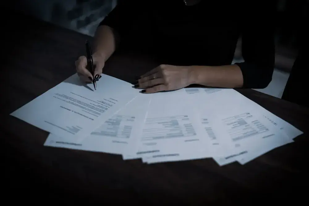 Comprador assinando contrato de imóvel às pressas com documentos espalhados na mesa