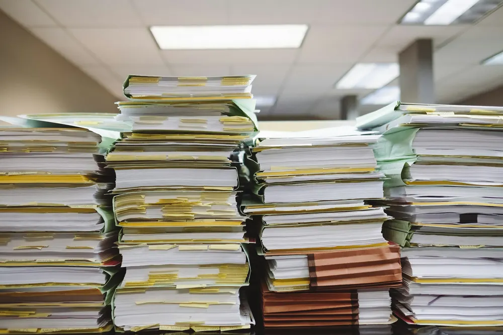 Pasta de documentos aberta sobre uma mesa, com papéis empilhados ao lado