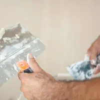 Mãos aplicando massa em uma parede com espátula