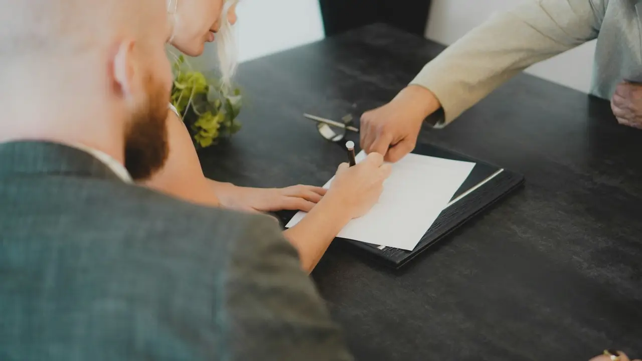 Casal assinando documentos de compra de imóvel sobre a mesa com calculadora