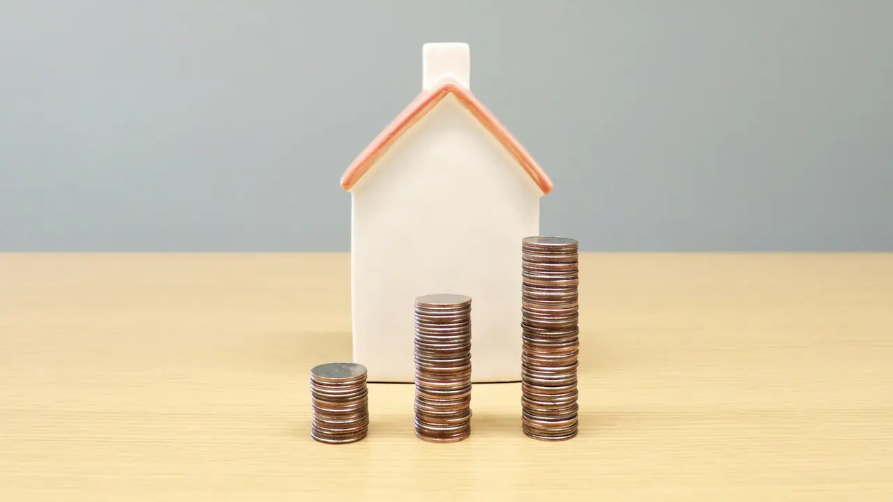 Miniatura de casa ao lado de pilhas de moedas crescentes, simbolizando o preço dos imóveis