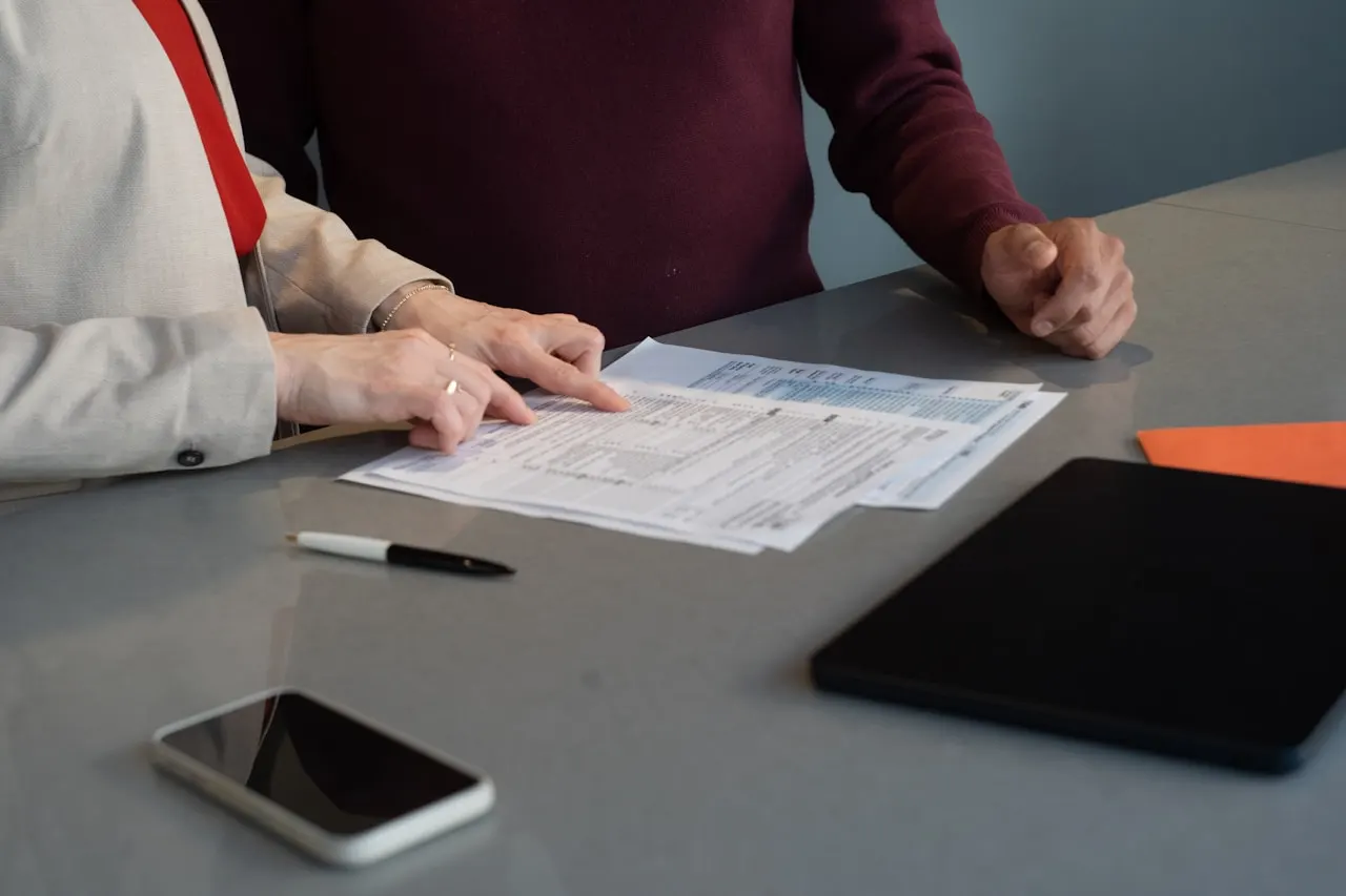 Duas pessoas analisando documentos impressos sobre a mesa de reunião