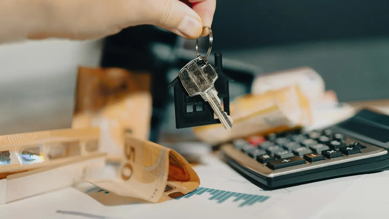 Mão segurando chave ao lado de calculadora e documentos, simbolizando o reajuste do aluguel